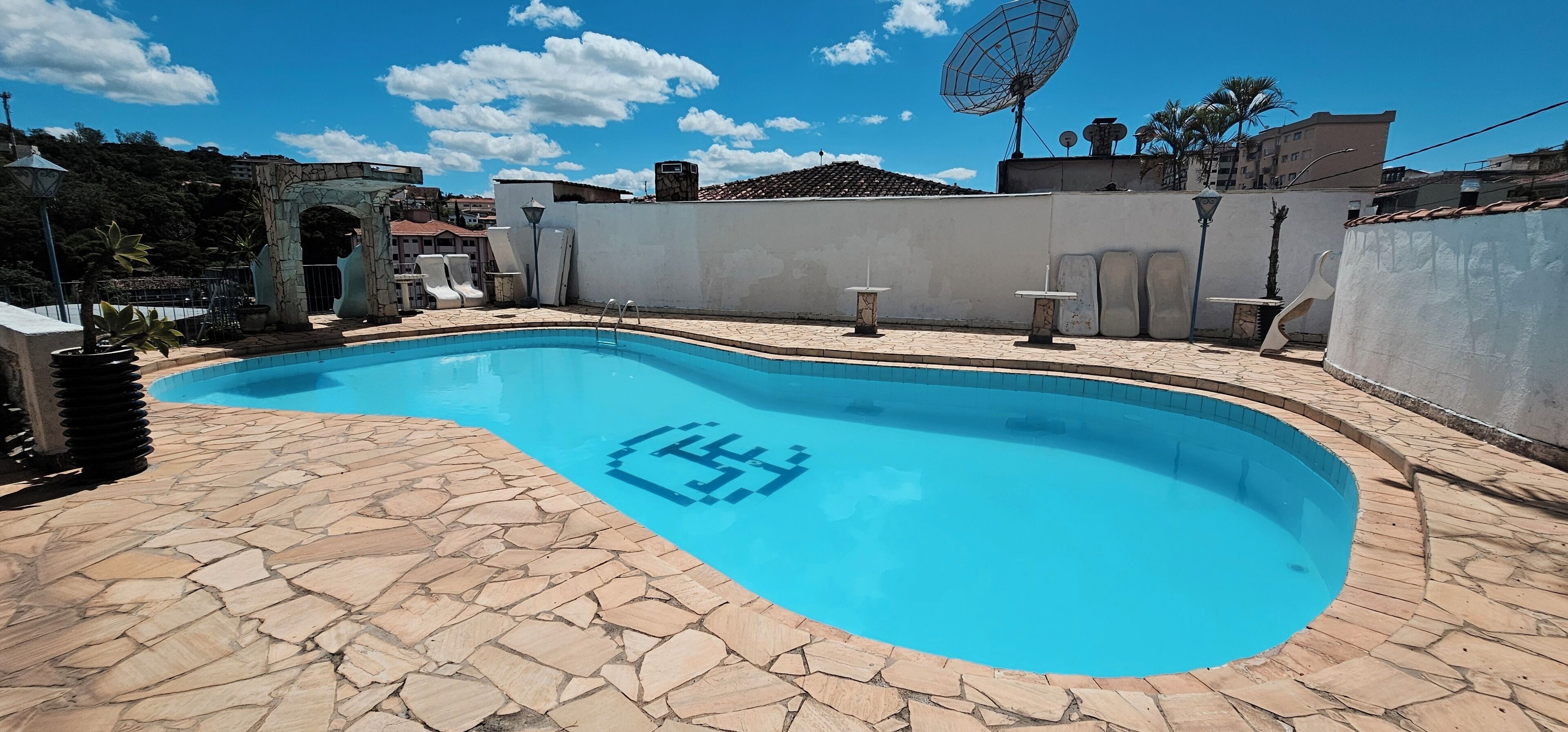 A swimming pool with a stone deck, a satellite dish, and a stone wall.