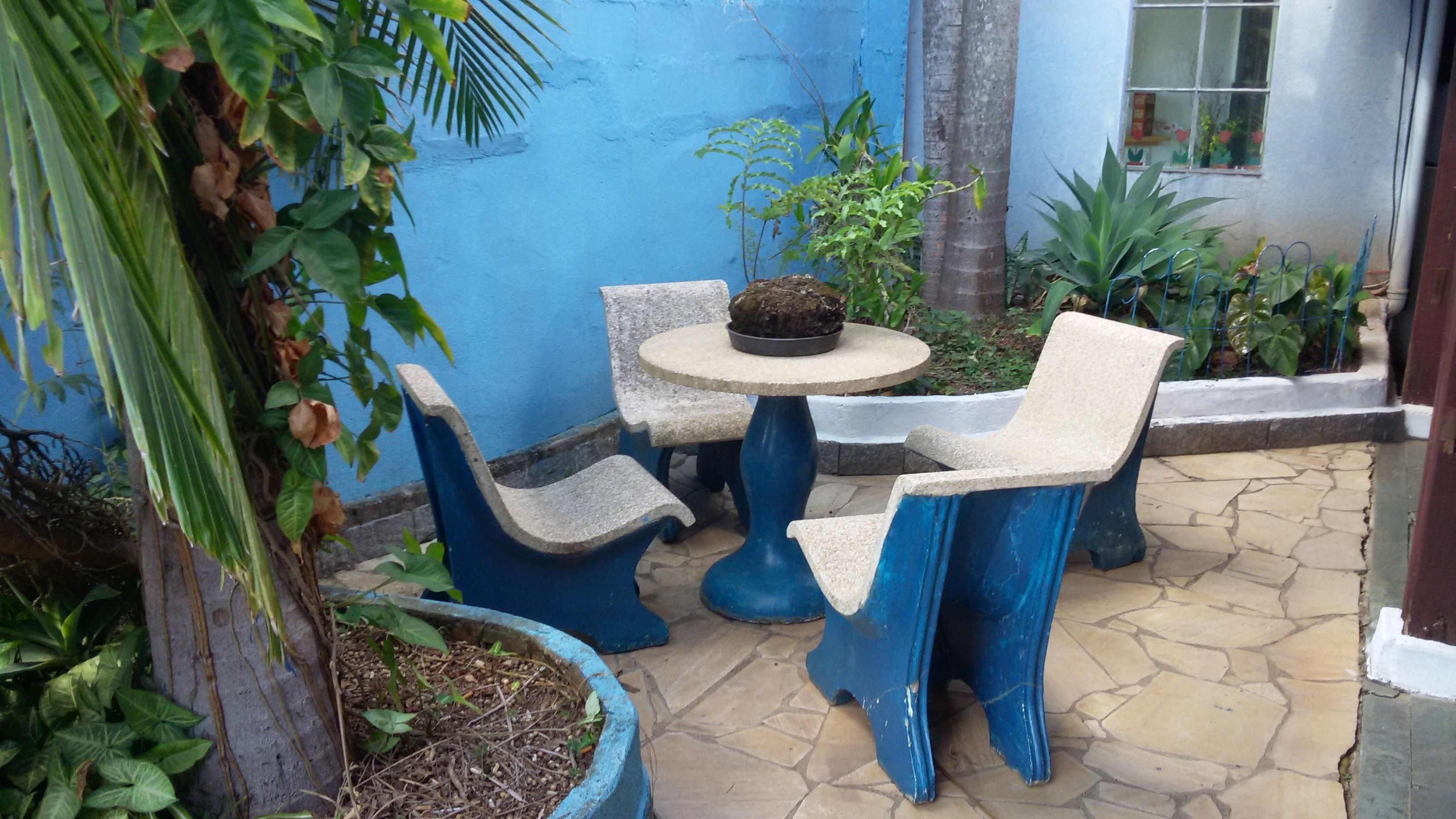 Un patio con un tavolo rotondo e due sedie, circondato da piante in vaso e un muro azzurro.