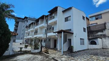 Um edifício residencial com vários andares, varandas, um pátio pavimentado e piso de pedra no térreo.