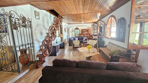 A cozy living room with a wooden ceiling, a sofa, a table, and a decorative wheel. - Hotel Pousada Casarão (Serra Negra)