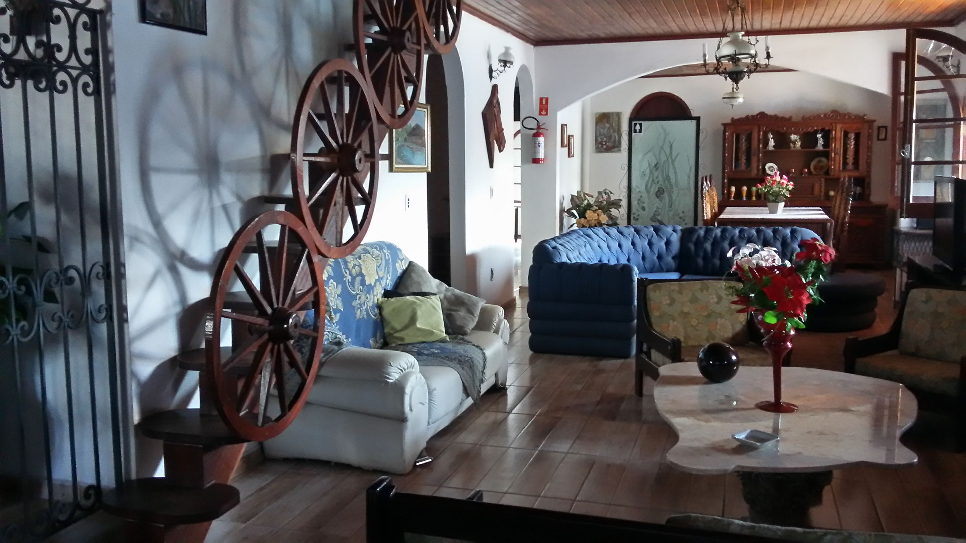 Uma sala de estar com um sofá, uma poltrona azul, uma mesa de centro de madeira e um objeto decorativo em formato de roda.