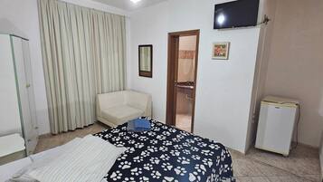 A hotel room with a bed, a chair, a television, a refrigerator, and a door leading to a bathroom.