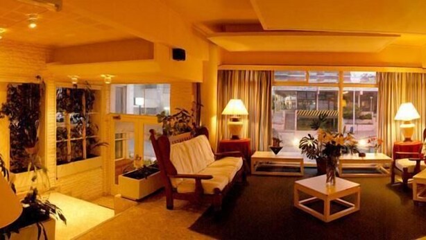 Un vestíbulo de hotel con un sofá, sillas, una mesa de centro y un ventanal con cortinas.