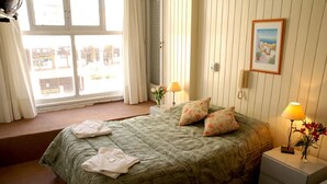 Un dormitorio con una cama, dos lámparas de noche, una mesita de noche, una ventana con cortinas y un cuadro en la pared.