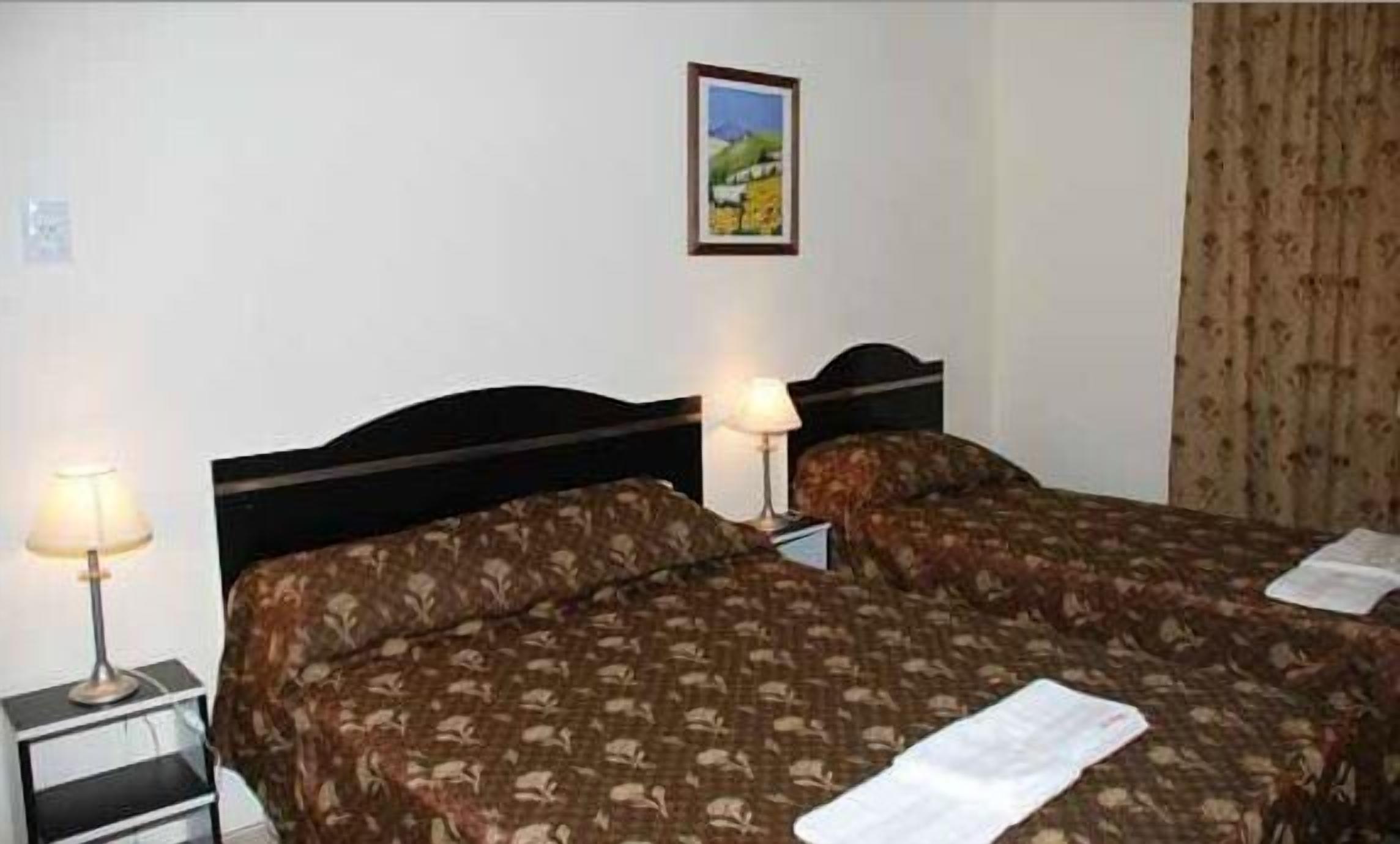 Una habitación de hotel con dos camas, una mesita de noche, una lámpara y un cuadro en la pared.