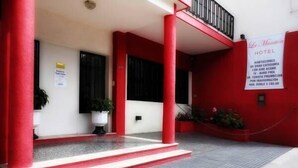 Fachada de hotel con pilares rojos, un cartel blanco y plantas en macetas.