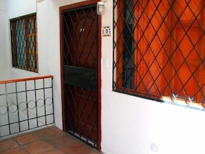 Une entrée fermée par un portail en métal, une fenêtre protégée par une grille en métal et une porte avec une plaque numérotée.