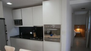 Una cuina moderna amb armaris blancs, un taulell negre, un microones, una cuina i un rentaplat.
