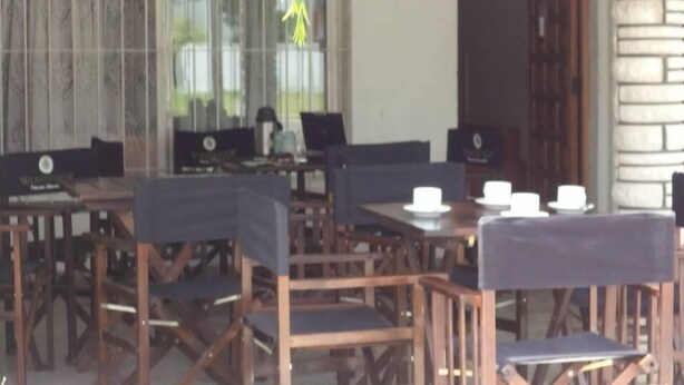 A covered outdoor seating area with wooden tables and chairs, a sign indicating a restaurant, and a stone wall. - Mar del Faro (Mar del Plata)