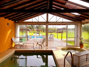 An indoor swimming pool area with a view of a grassy field and buildings in the background. - Pampas del Sur (Canuelas)