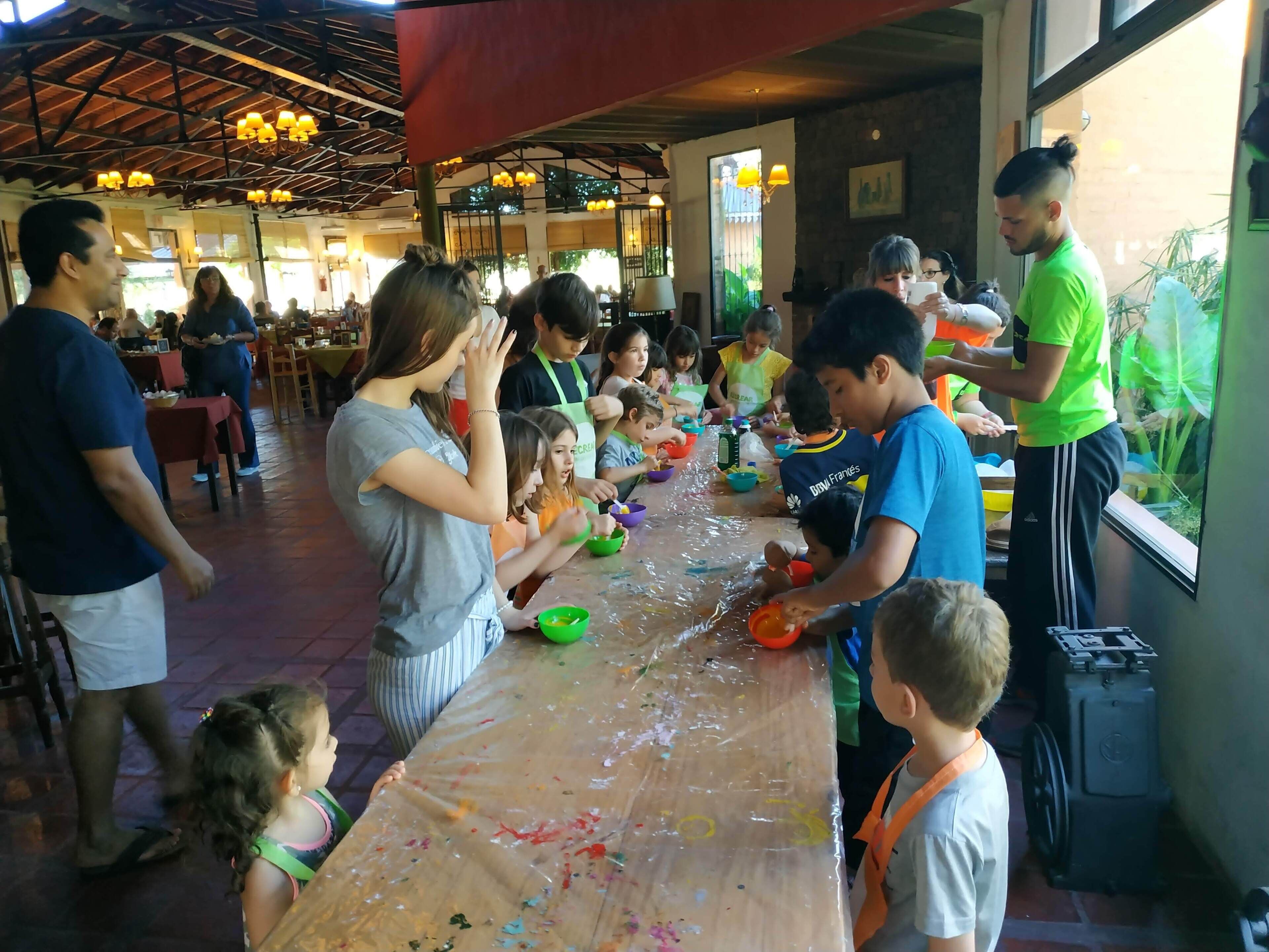 Un grupo de personas participa en una actividad en una mesa larga con diversos objetos y una ventana al fondo.