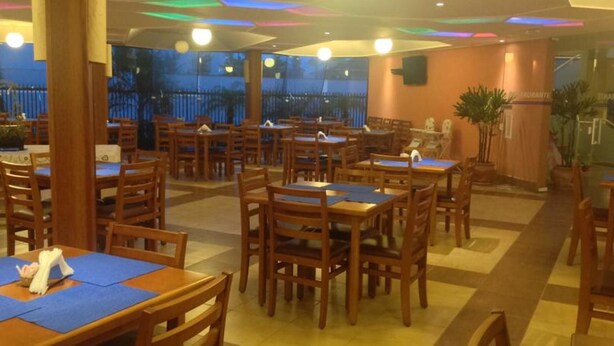 Un restaurante con mesas y sillas de madera, piso de baldosas y vistas al exterior a través de amplios ventanales.