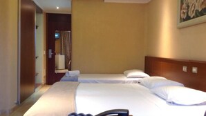 Habitación de hotel con dos camas, cabecera de madera, un cuadro en la pared y una puerta que da a otra habitación.
