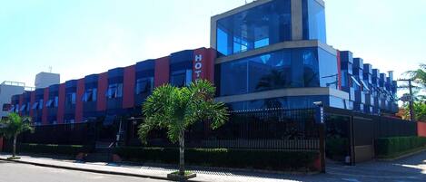 A modern hotel with a prominent glass facade, a red and blue color scheme, and a sign indicating it is a hotel.
