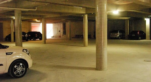 A multi-level parking garage with concrete pillars and a white car parked in the foreground. - Hotel Santamaria (Guarujá)