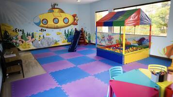 Une salle de jeux avec un sol coloré, une piscine à balles, un toboggan et une fresque représentant un sous-marin.