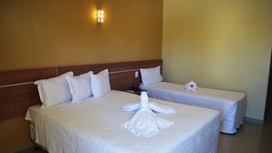 A hotel room with two beds, a wooden headboard, white bedding, a wall-mounted light, and a small table with a white object. - Pontal Praia Hotel (Porto Seguro)