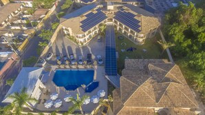 An aerial view of a resort with a central swimming pool, multiple guest rooms with solar panels, and a parking area. - Pontal Praia Hotel (Porto Seguro)