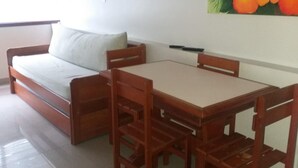 A room with a sofa, a dining table with chairs, and a painting of flowers on the wall. - Residencial Ilha Dourada (Florianópolis)
