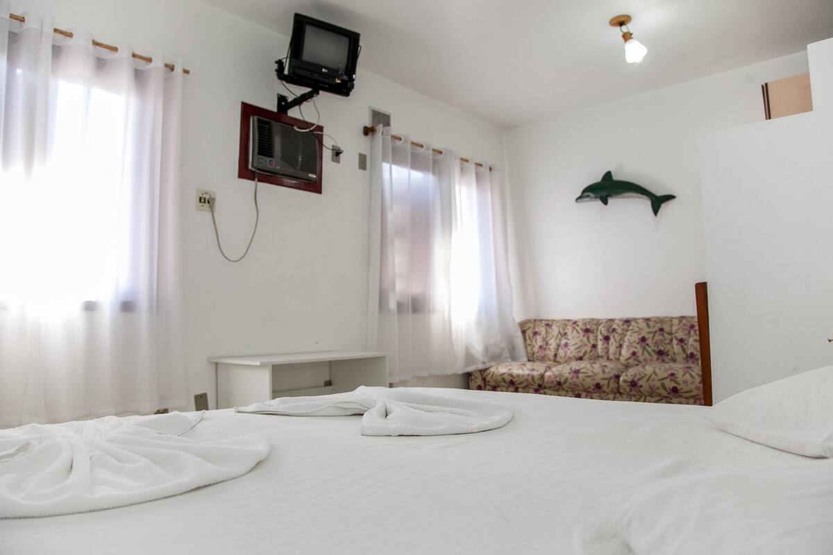 A hotel room with a bed, a television mounted on the wall, a desk, and a floral-patterned chair.