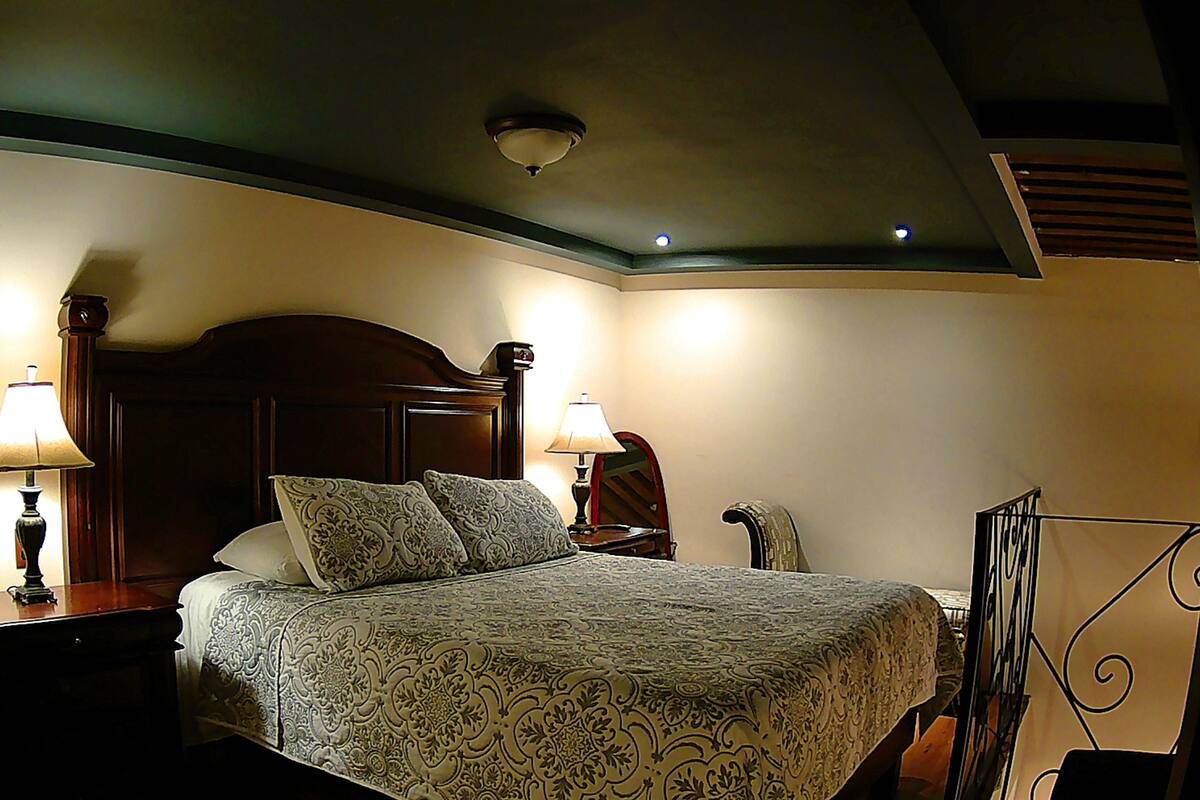 Une chambre d’hôtel avec un grand lit, deux tables de chevet avec des lampes, une tête de lit en bois et un luminaire au plafond.