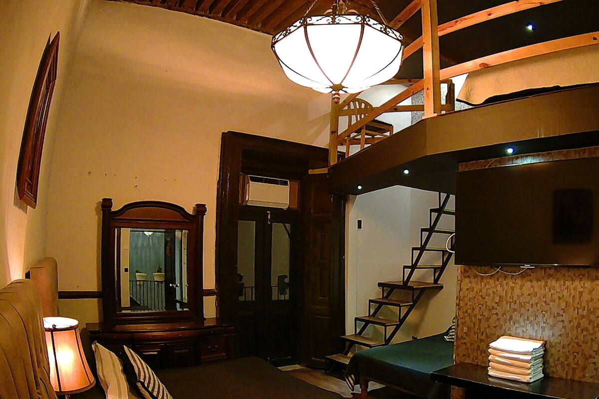 Une pièce comprenant un lit, une lampe, un miroir, un escalier et un téléviseur.