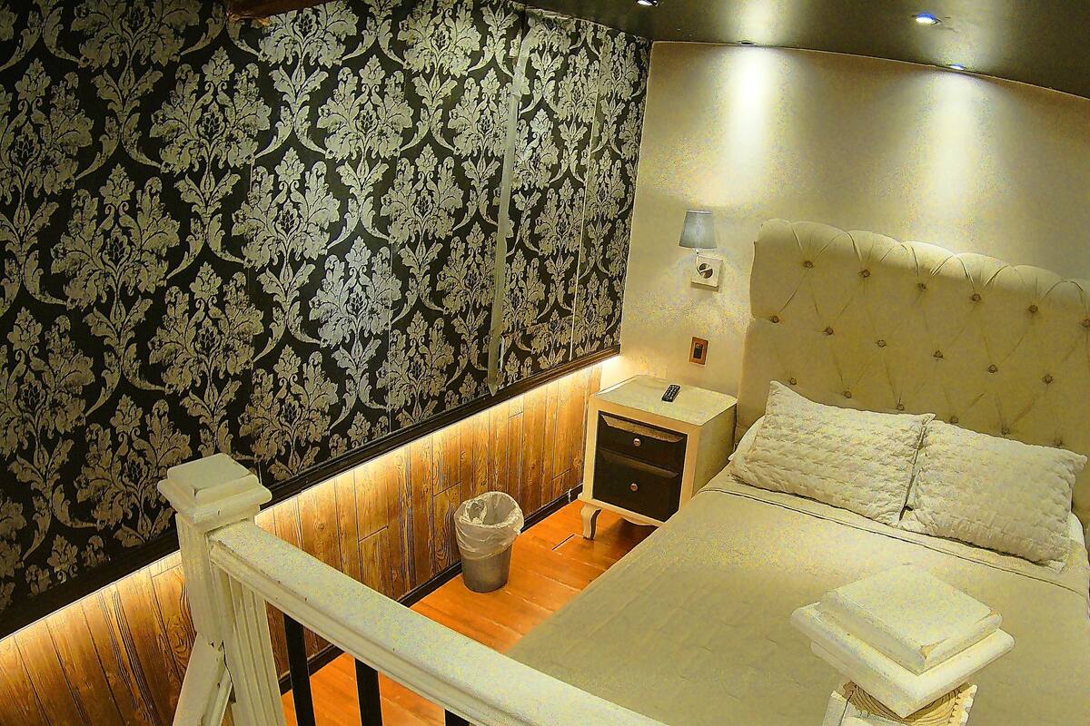 Une chambre à coucher avec un grand lit, une table de chevet, une chaise et une poubelle.