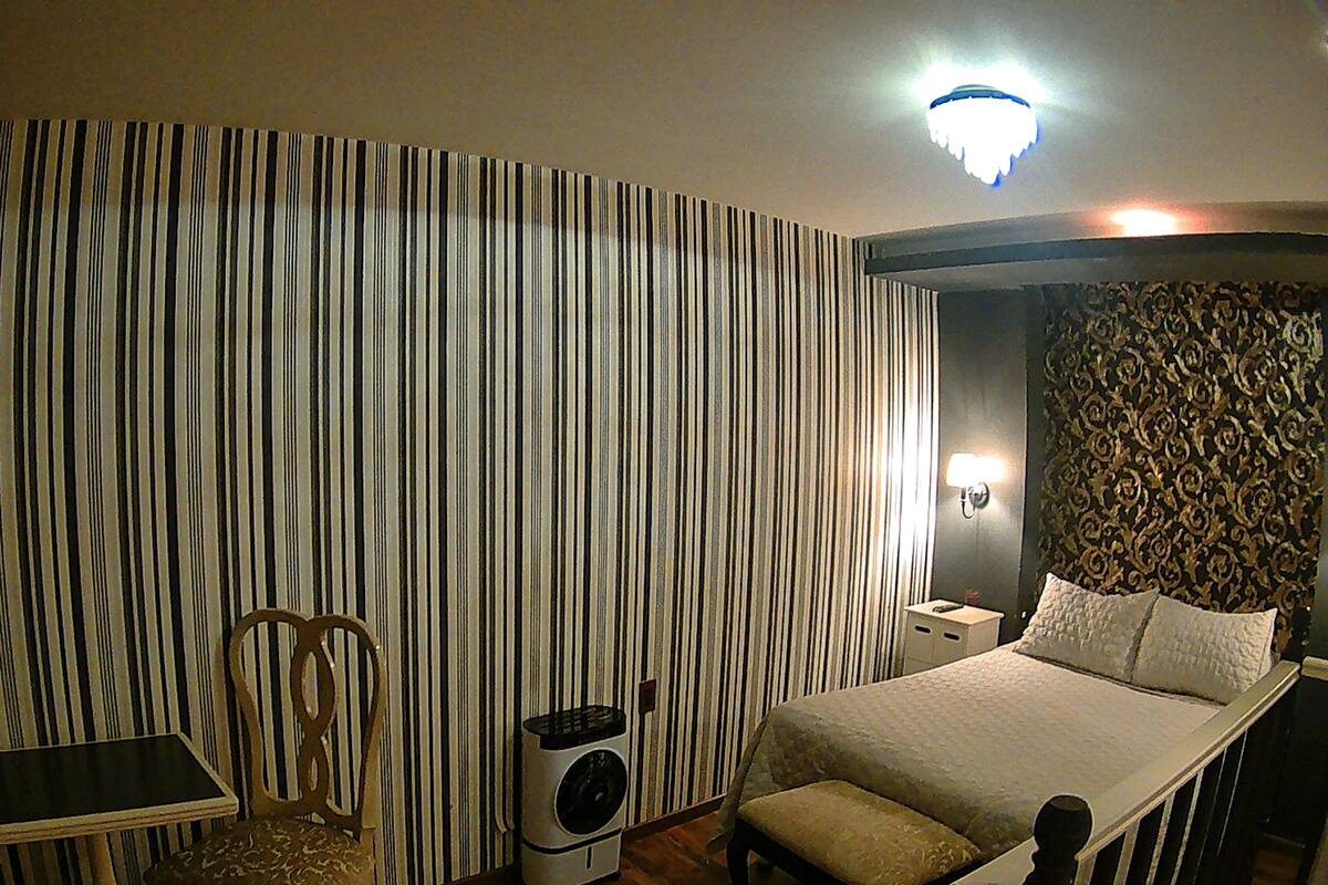 Une chambre d’hôtel comprenant un lit, une table de chevet, une chaise, un bureau et un mur orné de rayures verticales.