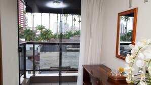 A balcony with a view of palm trees and buildings, a wooden table with a basket, and a vase of white flowers. - Hotel Príncipe (Joinville)
