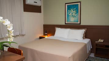 A hotel room with a bed, a nightstand, a lamp, a telephone, a painting on the wall, and a potted orchid.