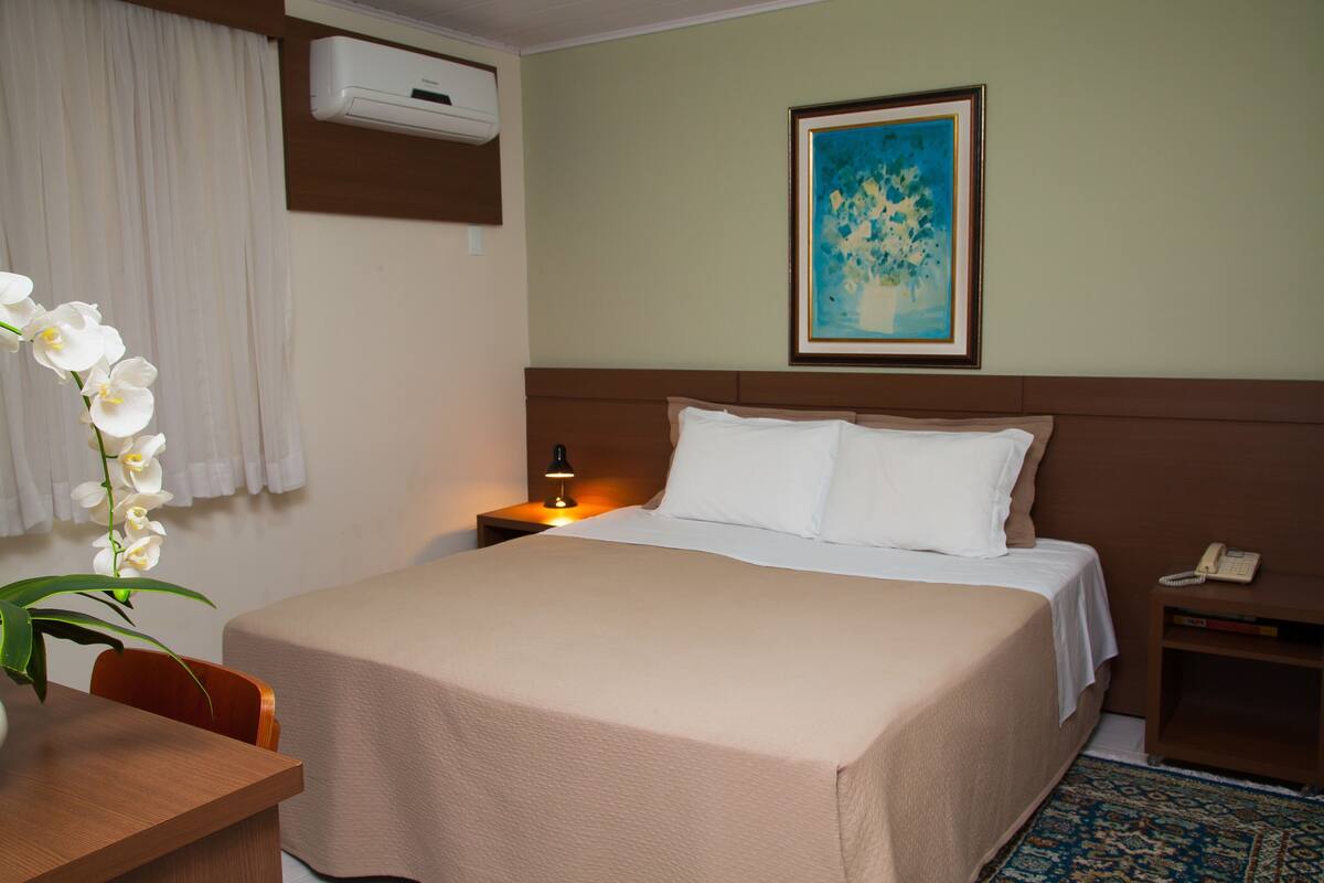 A hotel room with a bed, bedside lamp, nightstand, and a painting on the wall.