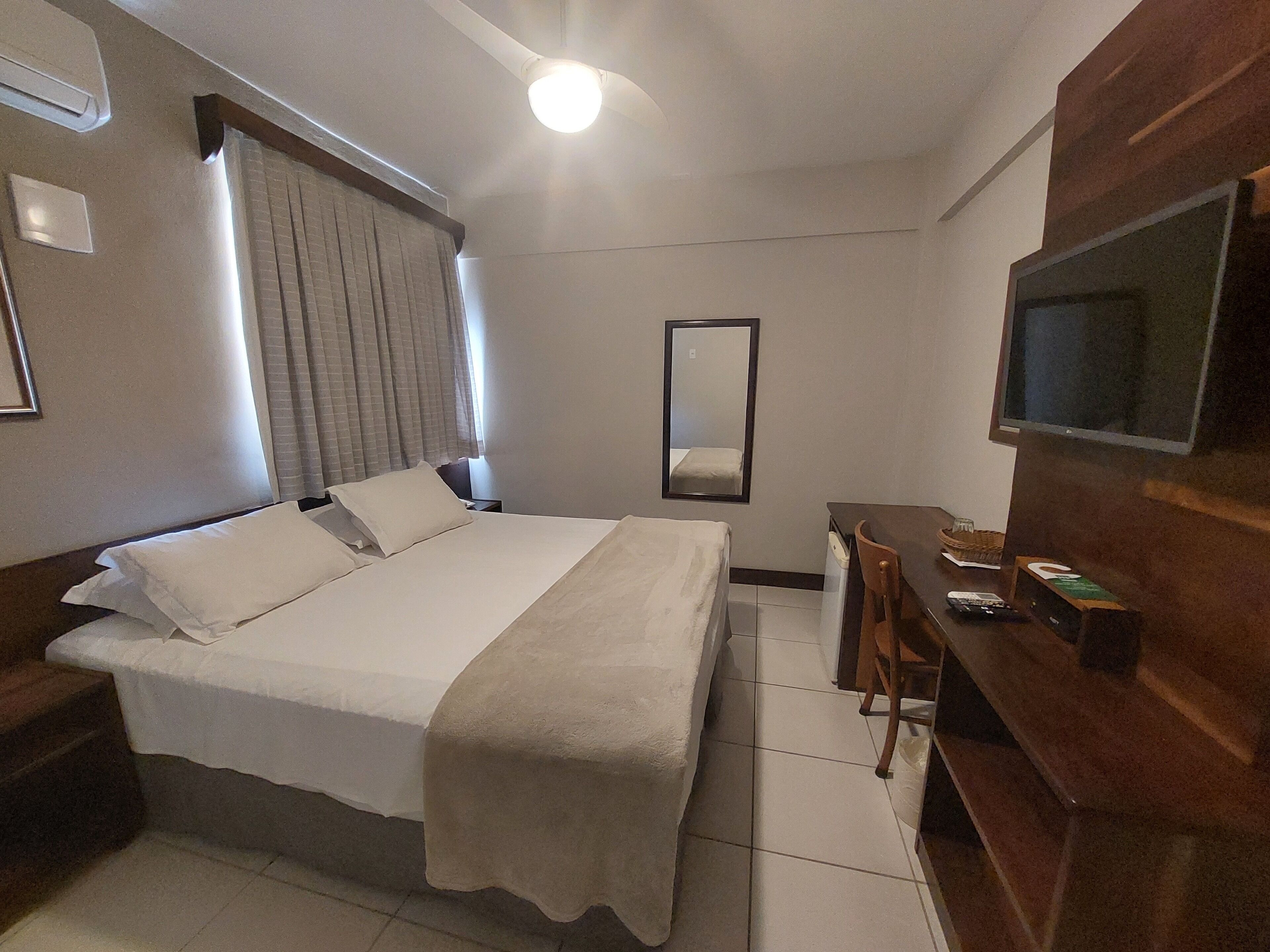 Una habitación de hotel con cama, escritorio, silla, televisión y espejo.