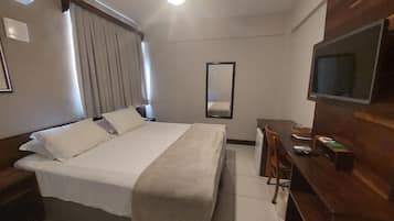 Una habitación de hotel con cama, escritorio, silla, televisión y espejo.