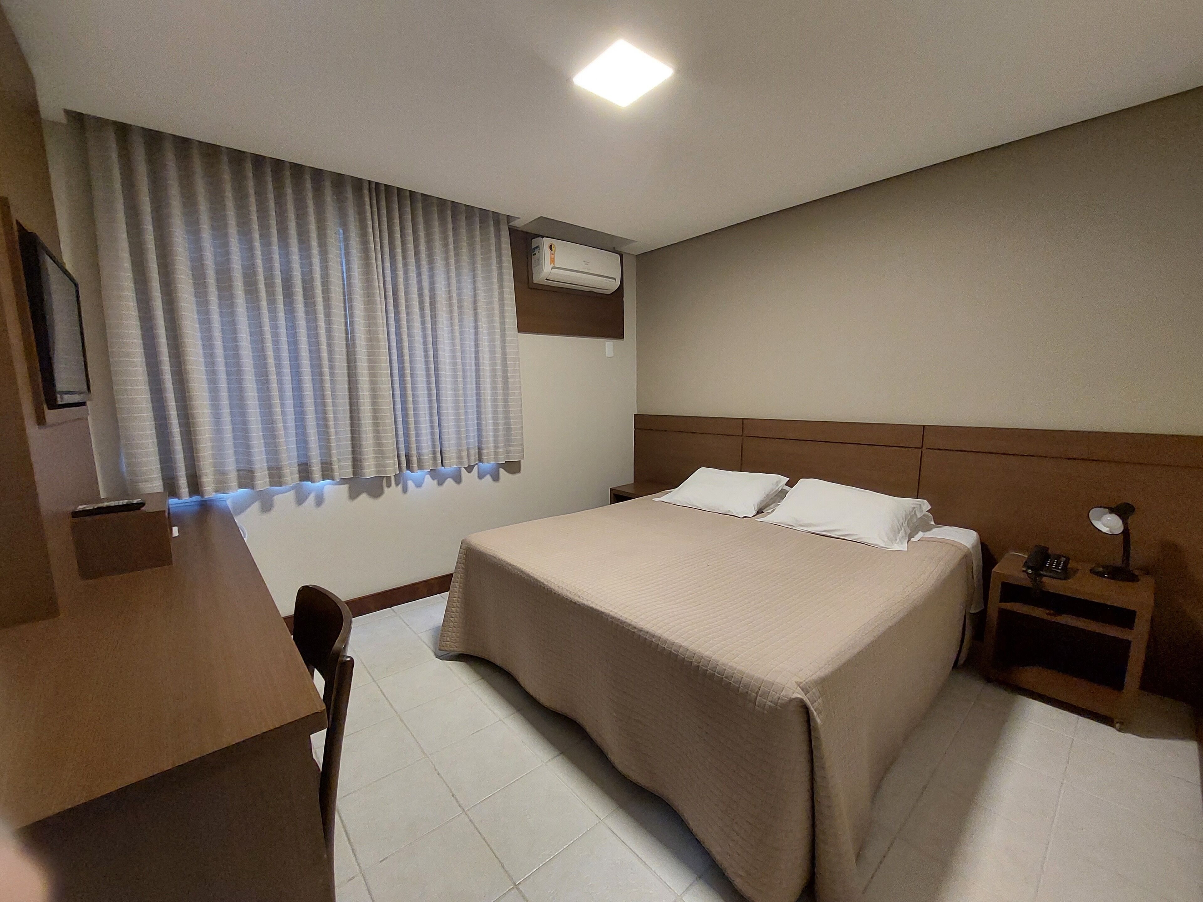 Una habitación de hotel con cama, mesita de noche, lámpara y aire acondicionado.