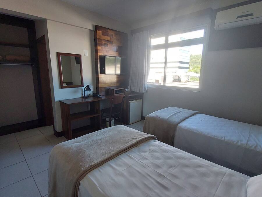 Habitación de hotel con dos camas, un escritorio con silla, un refrigerador pequeño, un espejo y una ventana con vista al exterior.