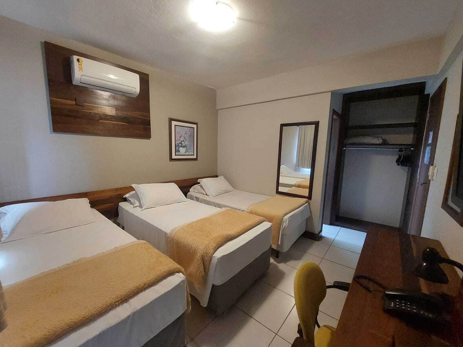 Een hotelkamer met twee eenpersoonsbedden, een bureau met stoel, een spiegel en een airconditioning.