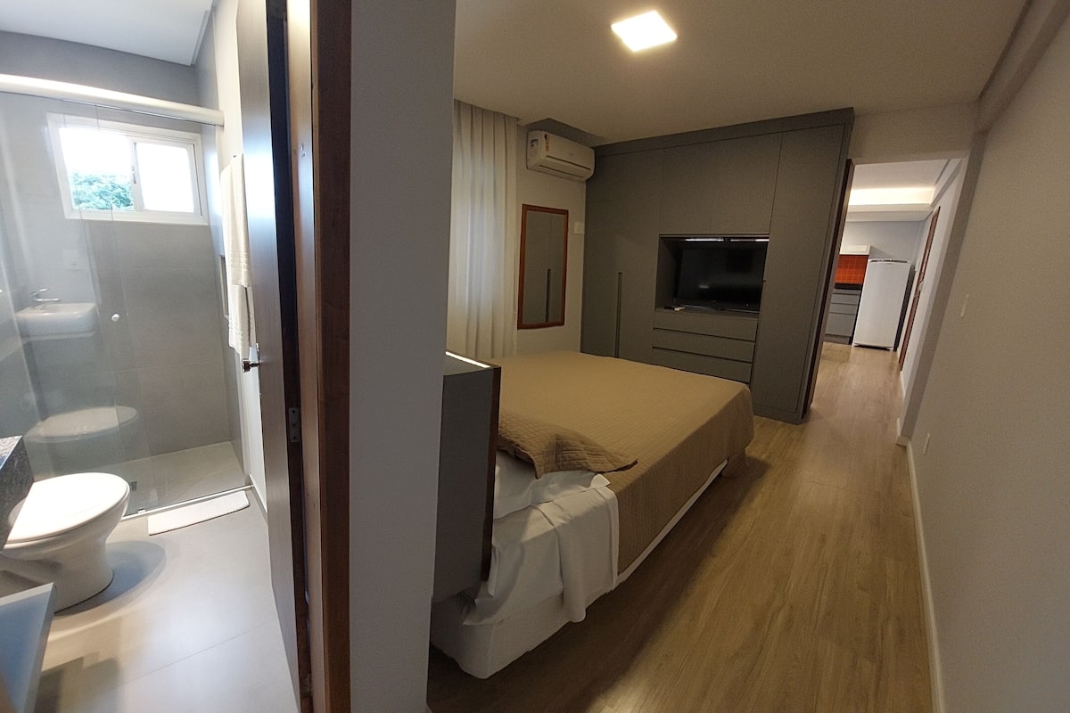 A compact hotel room with a shower, toilet, bed, TV, and kitchenette.
