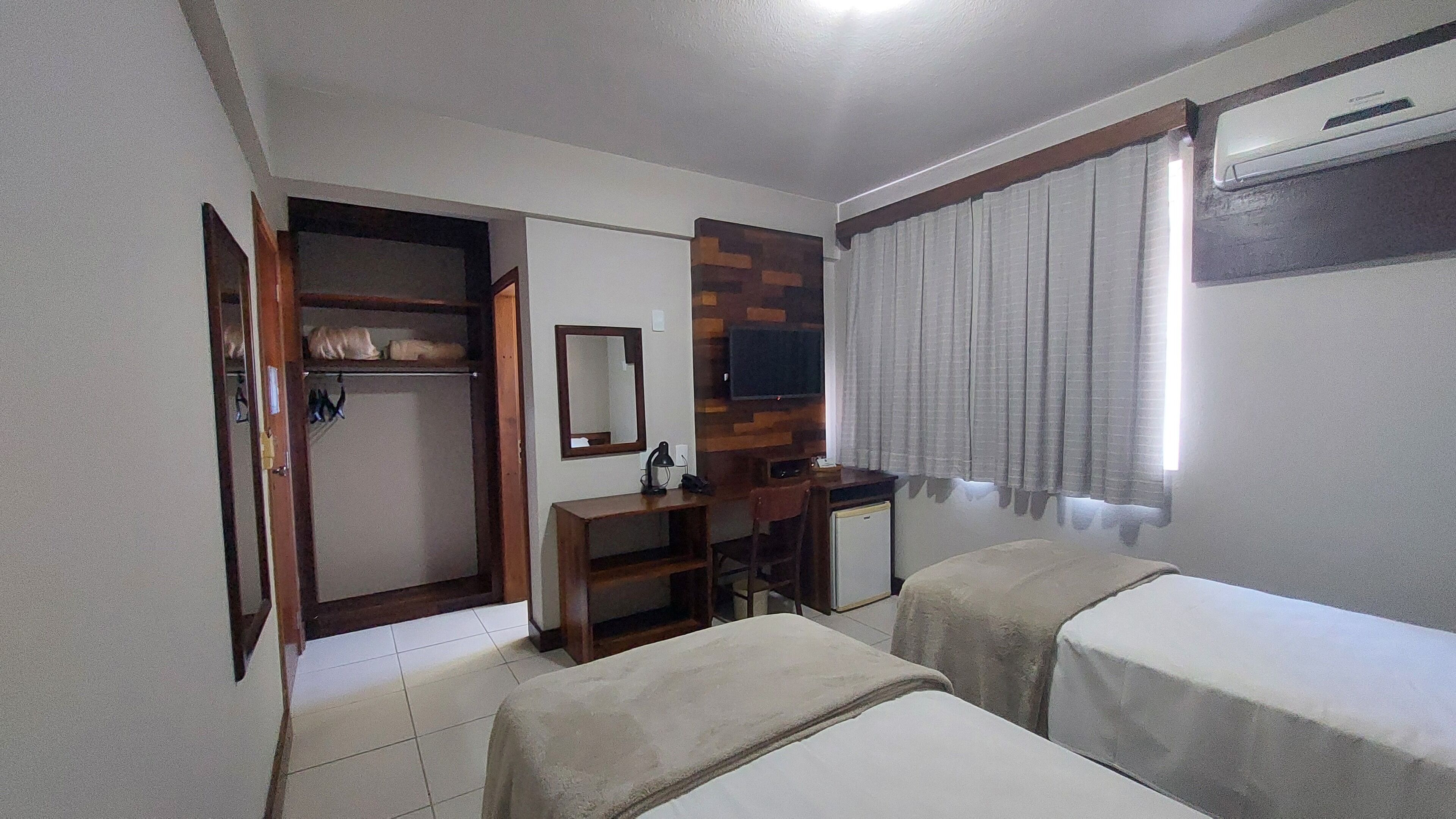 Habitació d'hotel amb llit, escriptori, cadira, televisió i armari.