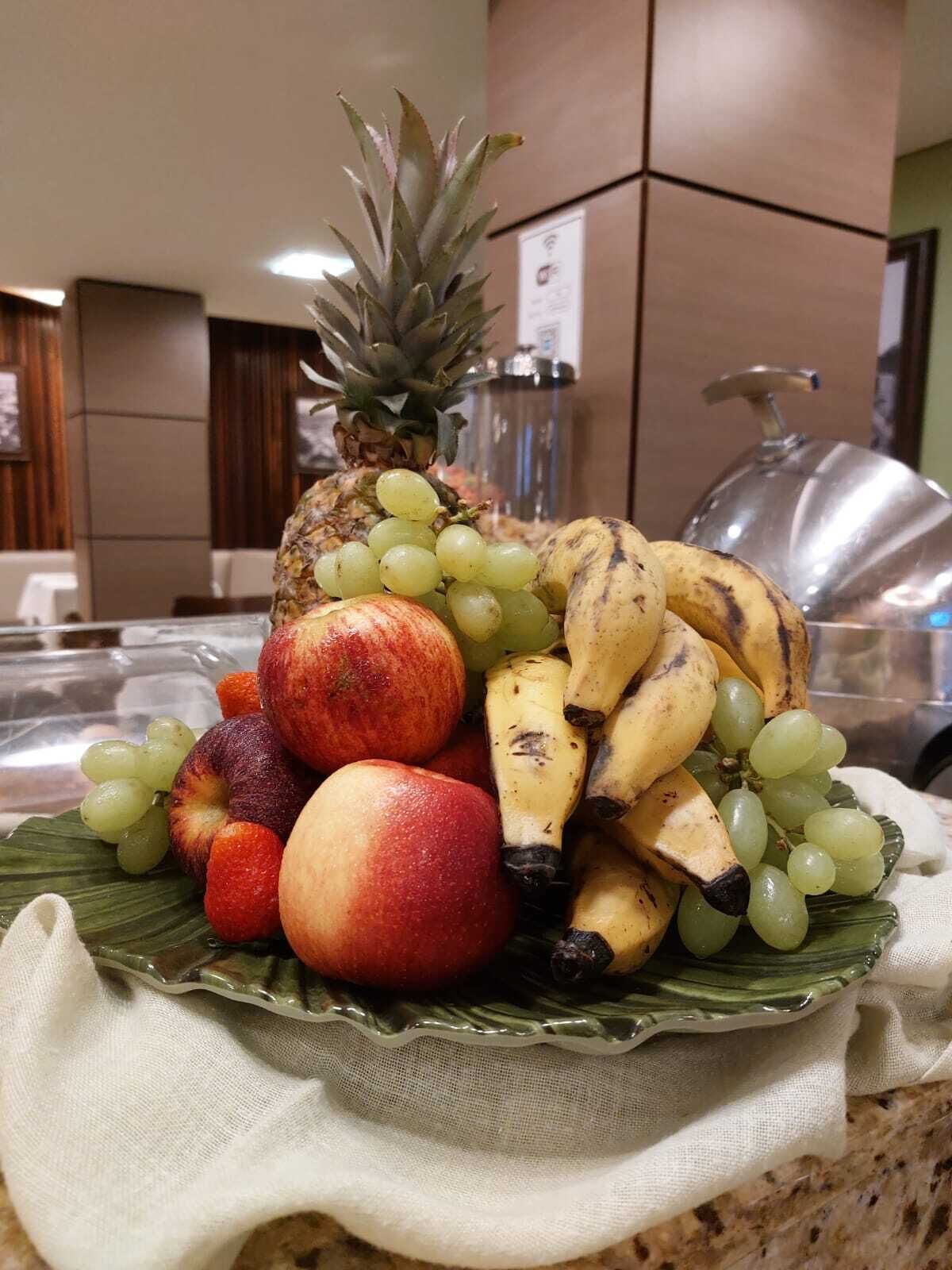 Una bandeja de frutas con piña, uvas, plátanos y manzanas sobre una mesa.
