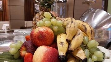 Una bandeja de frutas con piña, uvas, plátanos y manzanas sobre una mesa.