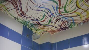 A bathroom with a bathtub, blue and white tiles, a shower, and a ceiling with colorful abstract patterns.