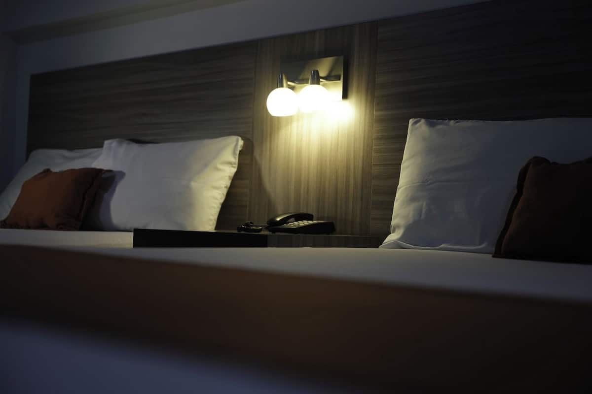 A hotel room with a bed, pillows, a bedside table, a lamp, and a telephone.