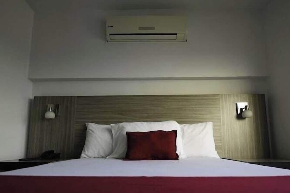 A hotel room with a bed, a headboard, an air conditioning unit, and two wall-mounted lamps.