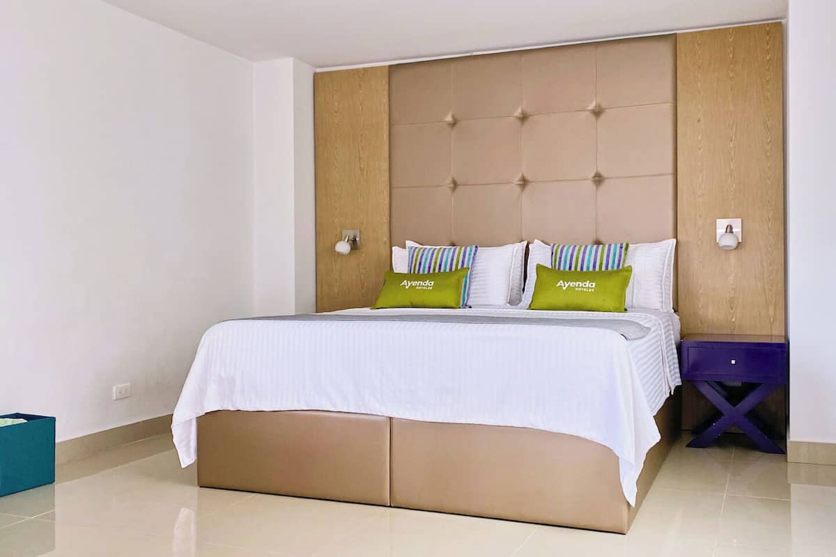 A hotel room with a bed, a wooden headboard, a nightstand, and a blue trash bin.