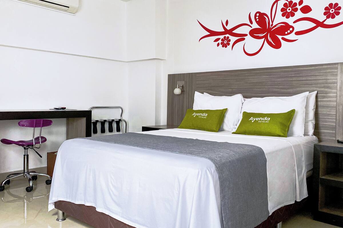 A hotel room with a bed, a desk, a chair, and a wall decoration.