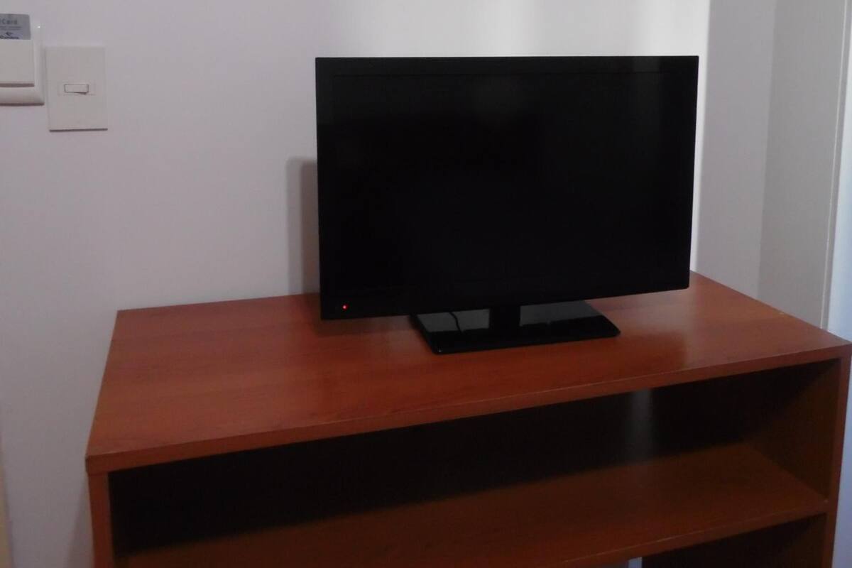 A flat-screen TV on a wooden TV stand with a shelf below.