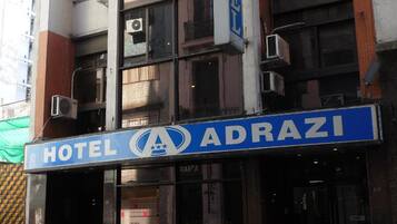 Un hotel llamado "HOTEL ADRAZI" con un letrero azul, ventanas amplias y varios equipos de aire acondicionado en el exterior.