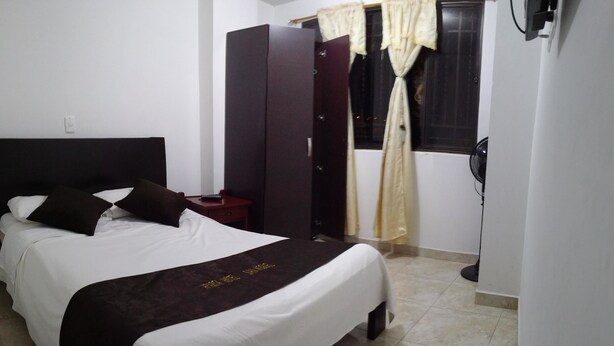 A neatly made bed with a white and dark brown bedspread, a dark headboard, and a bedside table with a lamp. - Apartahotel San Miguel (San Gil)