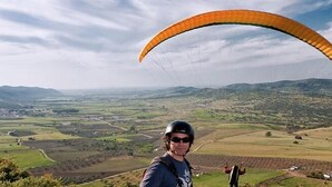 A person paragliding over a rural landscape with fields and hills. - Apartahotel San Miguel (San Gil)