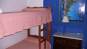 Una cama litera con una manta rosa, un pequeño aparador de madera y un mapa en la pared.